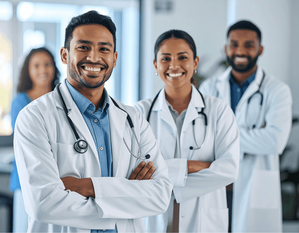 atendimento-cidadao-saude-publica-agil Fotografia de três profissionais de saúde sorrindo de braços cruzados, liderados por um médico com estetoscópio, representando uma equipe focada em um atendimento ao cidadão mais ágil e organizado na saúde pública.