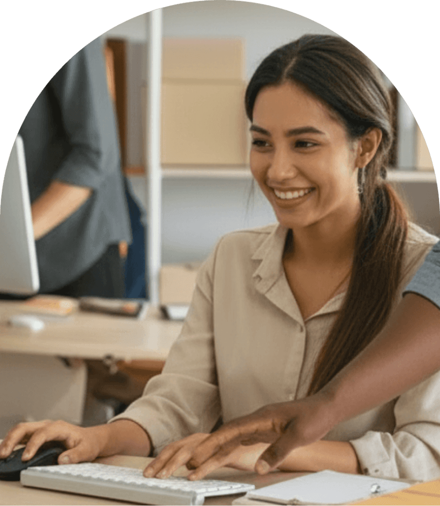 desafio-atendimento-varejo-tempo-resposta-vendas Retrato de uma mulher sorrindo enquanto digita no teclado de um computador em um ambiente de estoque, emoldurada com cantos arredondados, acompanhando o texto sobre o desafio de evitar a perda de oportunidades de venda por demora na resposta ao cliente.