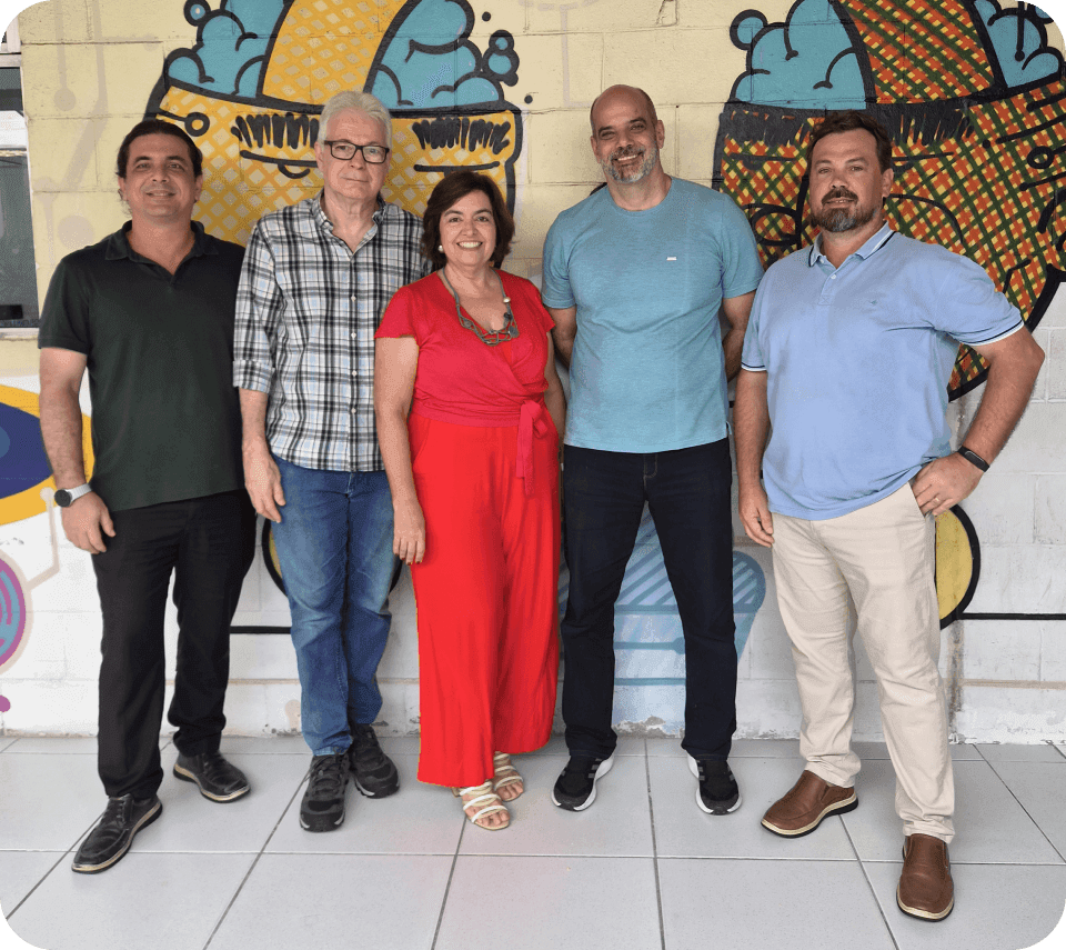 diretoria-fundadores-tactium-trajetoria-inovacao Fotografia de cinco profissionais líderes da Tactium posando juntos em frente a uma parede com arte urbana, simbolizando as relações duradouras e a trajetória guiada por inovação desde 1996.